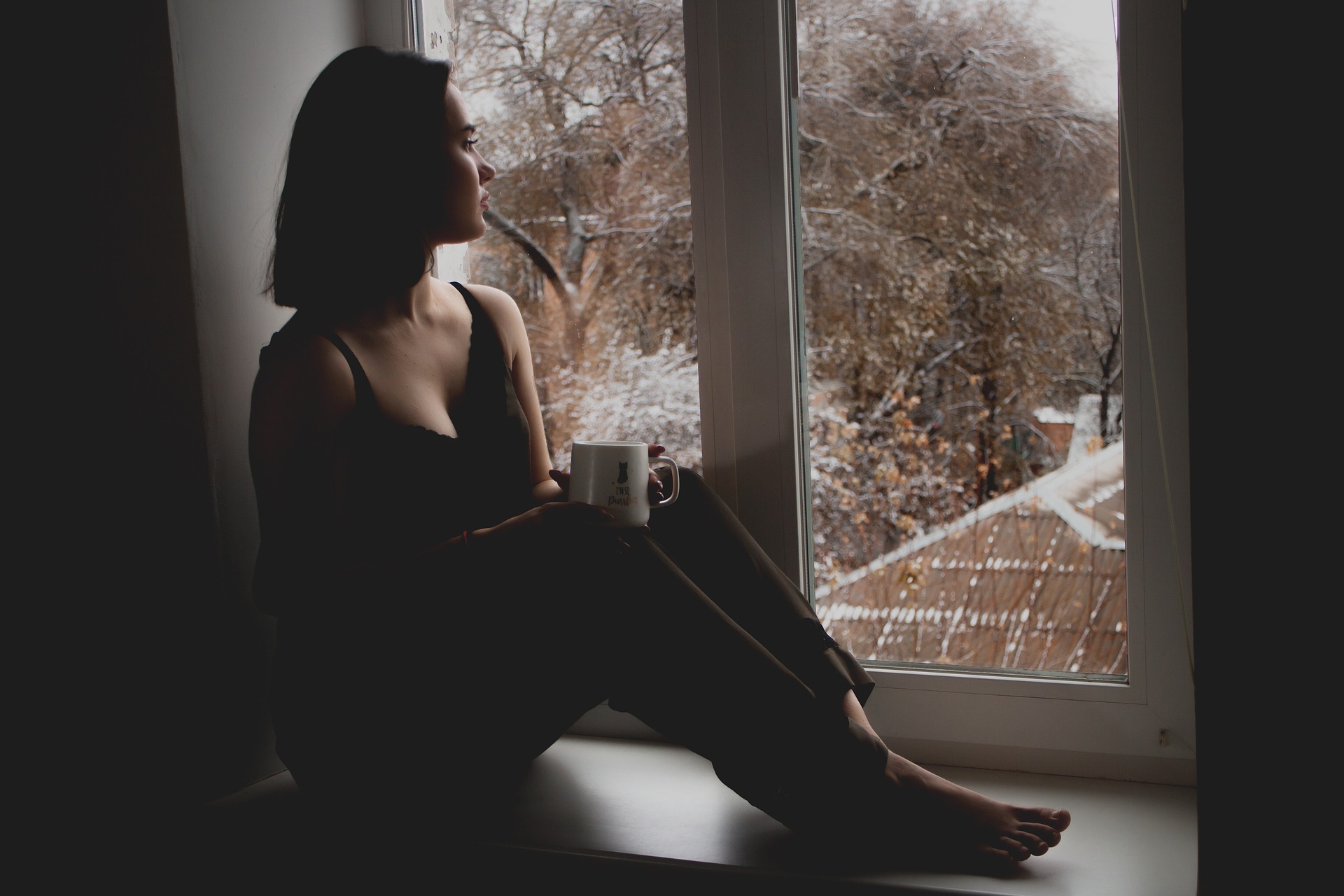 young woman sitting on a window ledge and gazing out on a bare tree